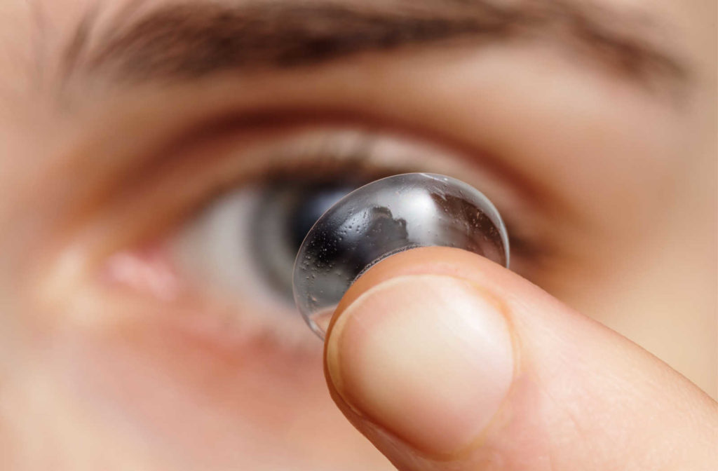 A close-up of a wide contact lens on the tip of a finger and about to be put into the eye.