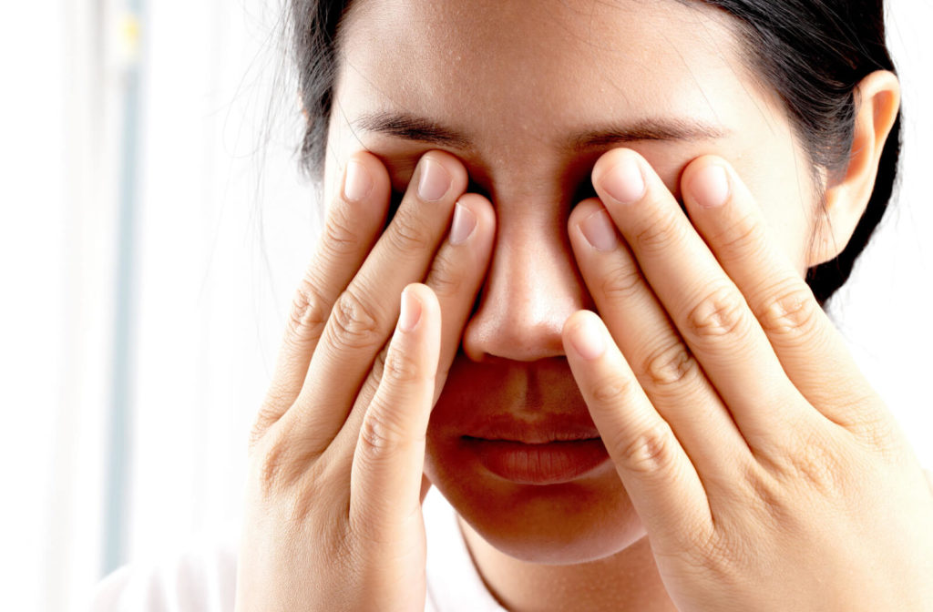 A woman experiencing eye floaters and frequent flashes of lights is covering her eyes and massaging to regain her vision.