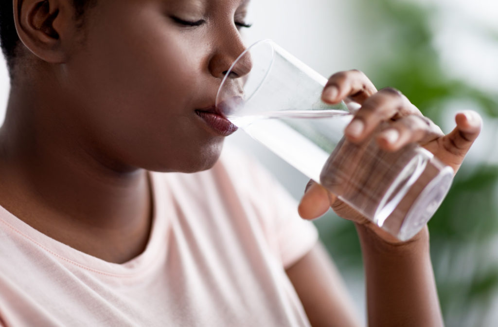 A young woman drinking a glass of water and closing her eyes.