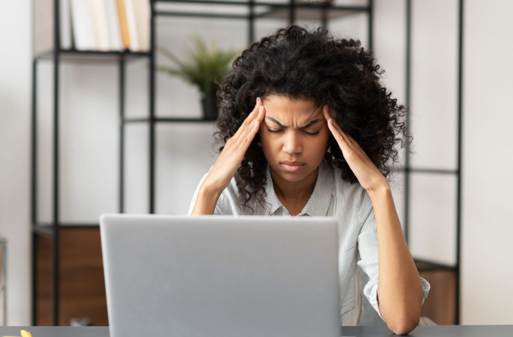 A stressed young woman who is experiencing a severe headache tries to alleviate the pain by applying pressure to her temples.