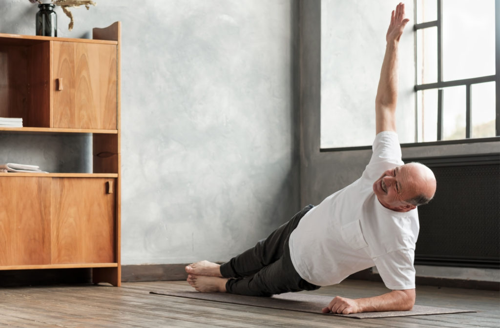 An energetic senior man doing yoga in a brightly lit room.