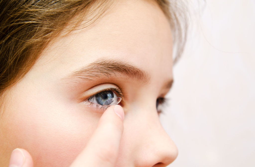 A young girl putting on a contact lens on her right eye.