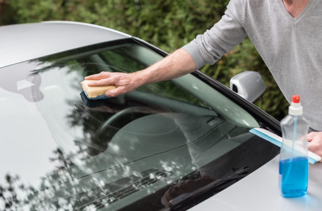 A man cleaning the windshield of his car using a sponge.