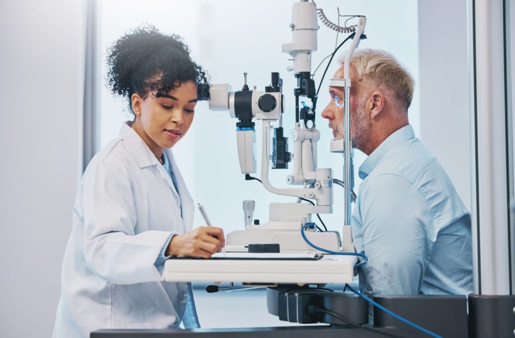 An optometrist taking notes while examining a senior's eyes to find out if his cataracts are returning.