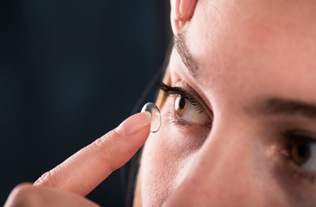 A close-up image of a woman putting a contact lens in her eye after waiting for an eye infection to clear up.