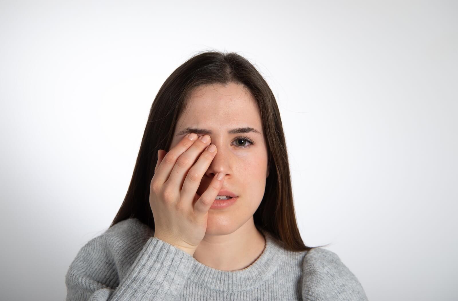 Woman holding her hand over one eye, showing discomfort possibly due to eye irritation or a scratched cornea.