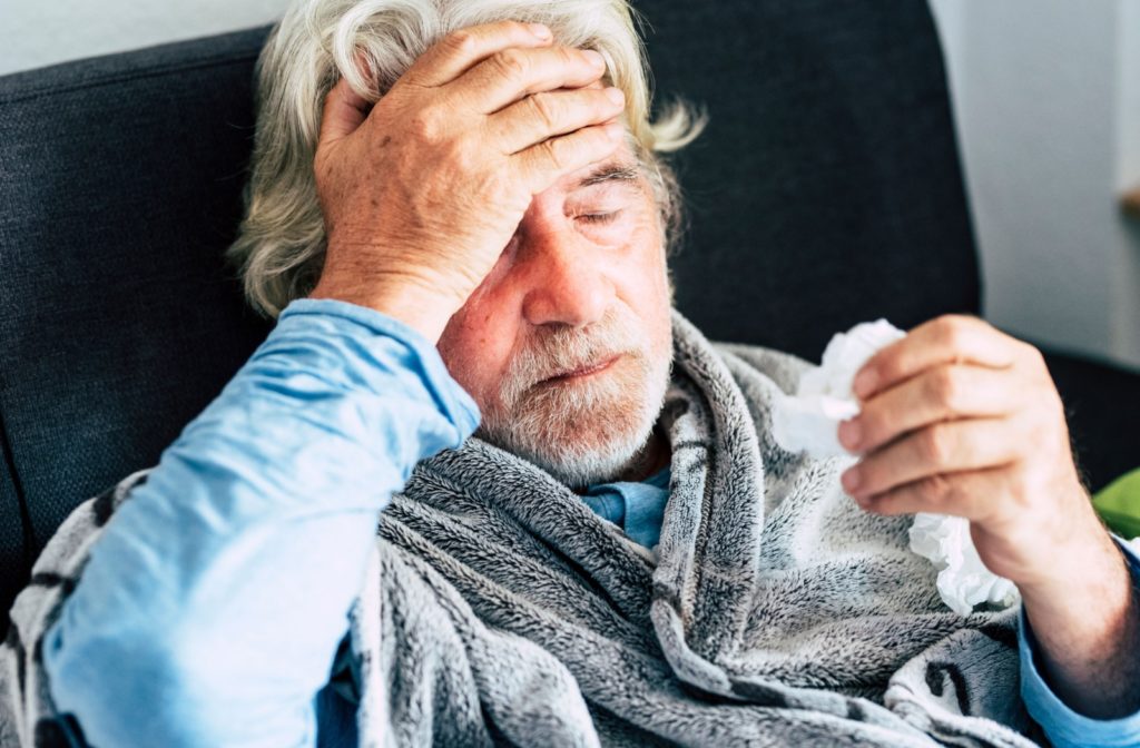 A sick person with a headache lying in bed with their eyes closed.