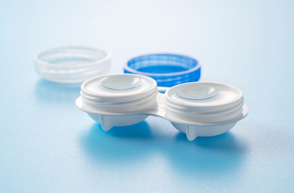 A close-up of a white contact lens case with soft contact lenses inside, placed on a light blue surface.
