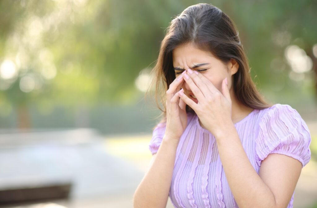 Woman outdoors with hands over her eyes, experiencing discomfort from allergies.