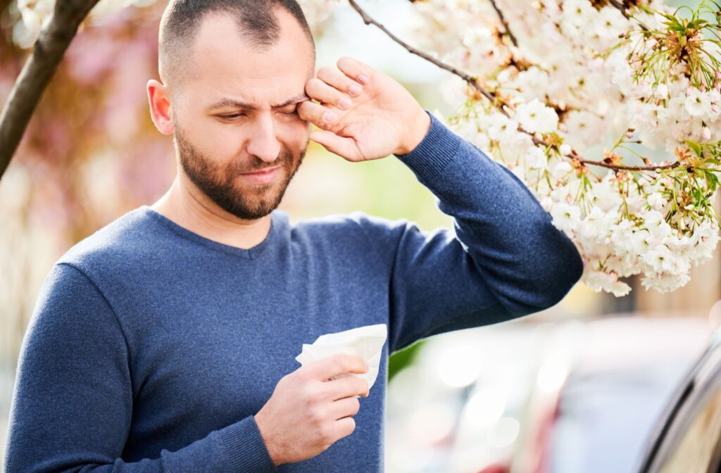 A man standing outside, wiping his eye with the back of his hand due to allergy and dry eye symptoms