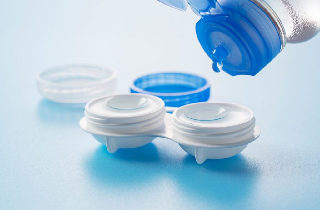 A close up of contact lenses in a contact case with a bottle of contact lens solution being squeezed into the contact lens case.