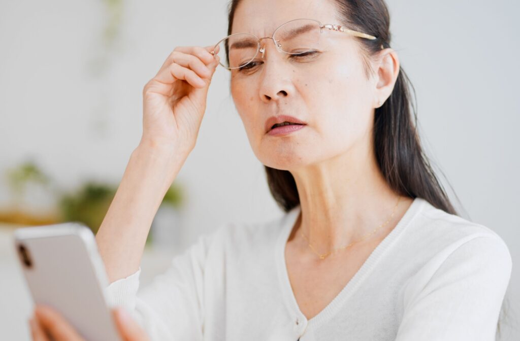 A woman lifting up her glasses, struggling to see what is on her phone close up.