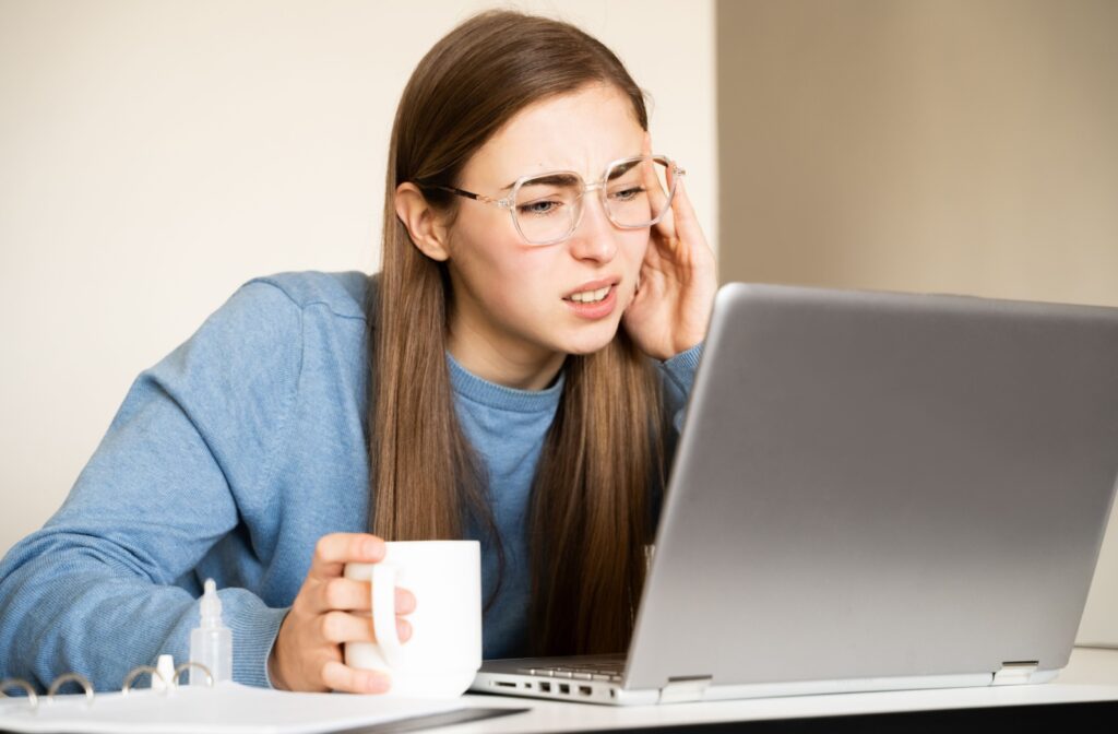 A person holding the side of their head while looking at a laptop screen, experiencing eye strain from digital screens.